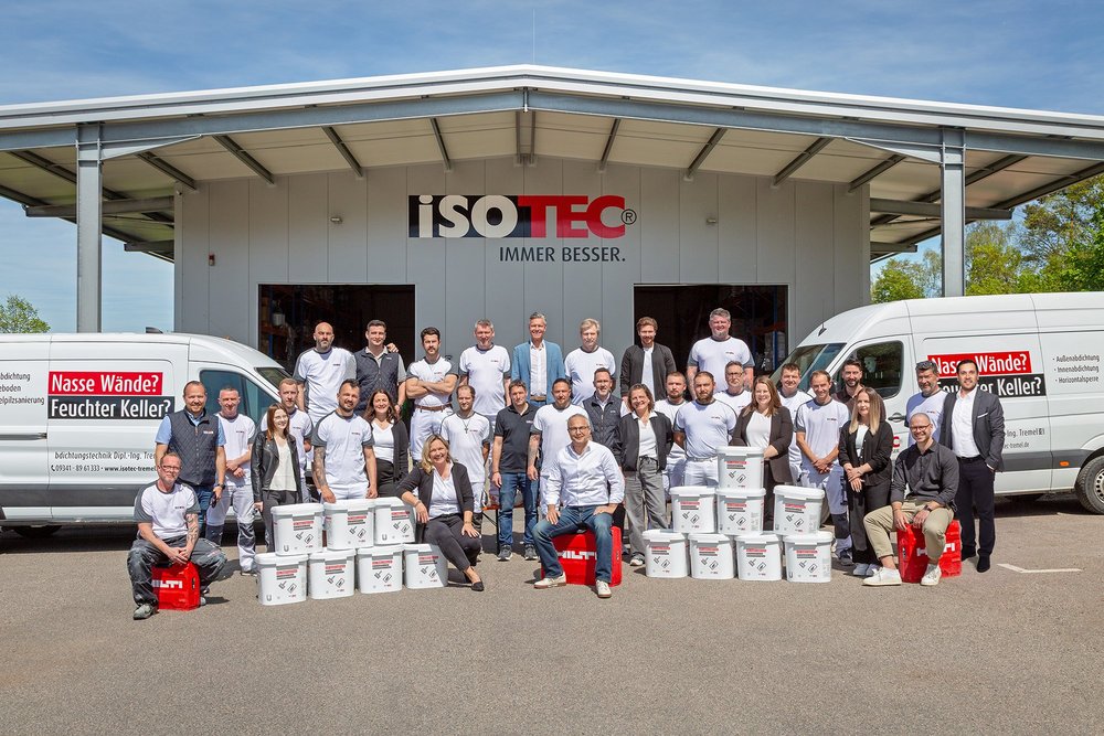 ISOTEC Teamfoto vor Firmenhalle mit Transportern und gestapelten Materialeimern.