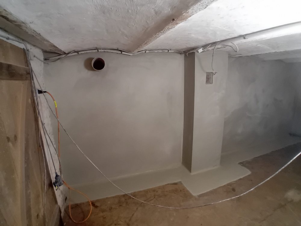 Kellerraum mit frisch beschichteter Wand, sichtbaren Kabeln an der Decke und rundem Rohrdurchlass.