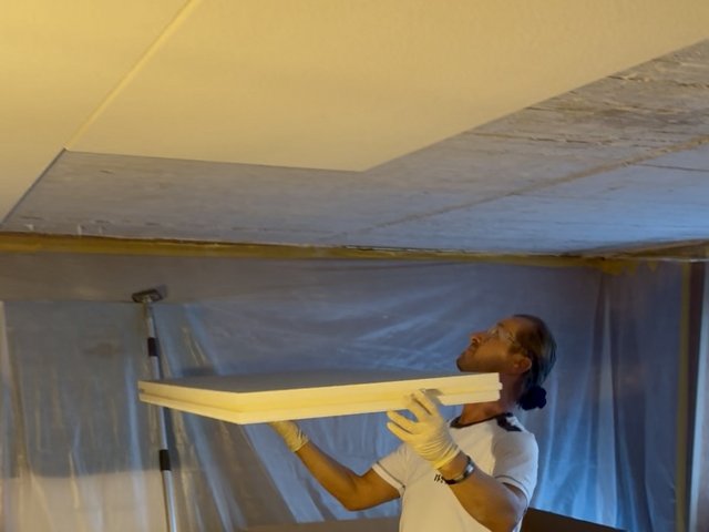 Arbeiter hält helle Platte an eine abgehängte Decke, Folienabdeckung im Raum.