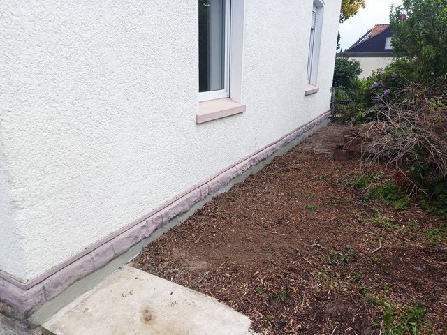 Weiße Hausfassade mit freigelegtem Erdstreifen am Sockel