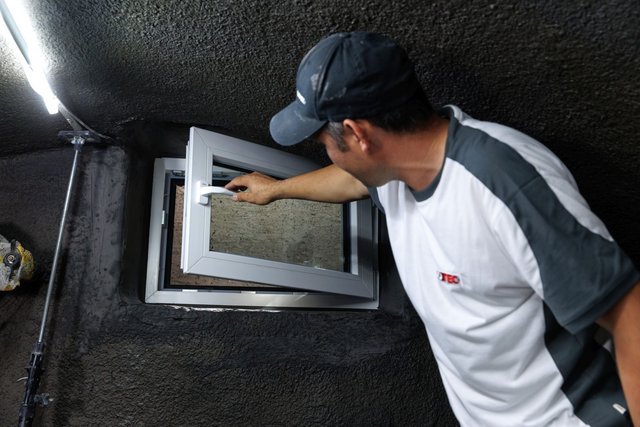 ISOTEC Mitarbeiter öffnet Kellerfenster in schwarz beschichteter Wand