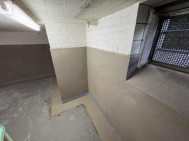 Kellerwand-Ecke mit weißem Mauerwerk, grauer Masse und Gitterfenster