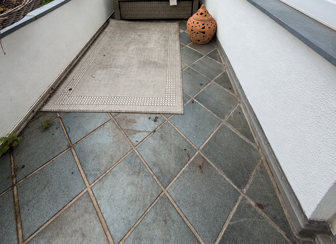 Balkon mit Rattansessel und Holzliegestuhl auf grau gefliestem Boden