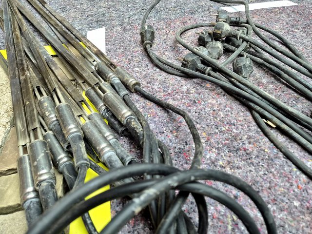 Bündel Metallstäbe und schwarze Stromkabel mit Steckern auf Filzschutzmatte