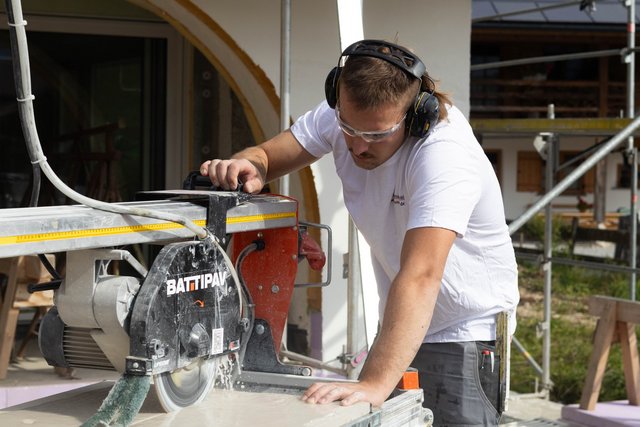 Arbeiter schneidet helle Platte mit Nassschneider und trägt Schutzbrille und Gehörschutz.