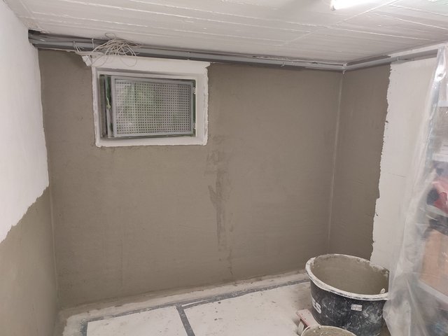 Kellerraum mit grauer Masse an der Wand, kleines Fenster und Kabelkanal an der Decke.