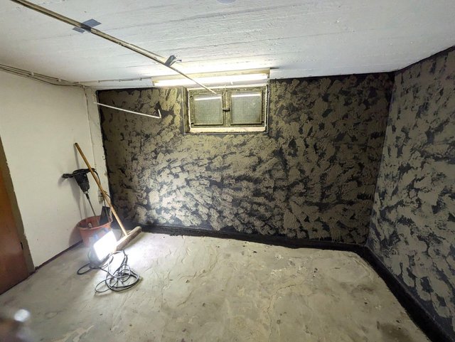 Kellerraum mit rauer grauer Masse an Wand, kleines Fenster, Baustrahler am Boden