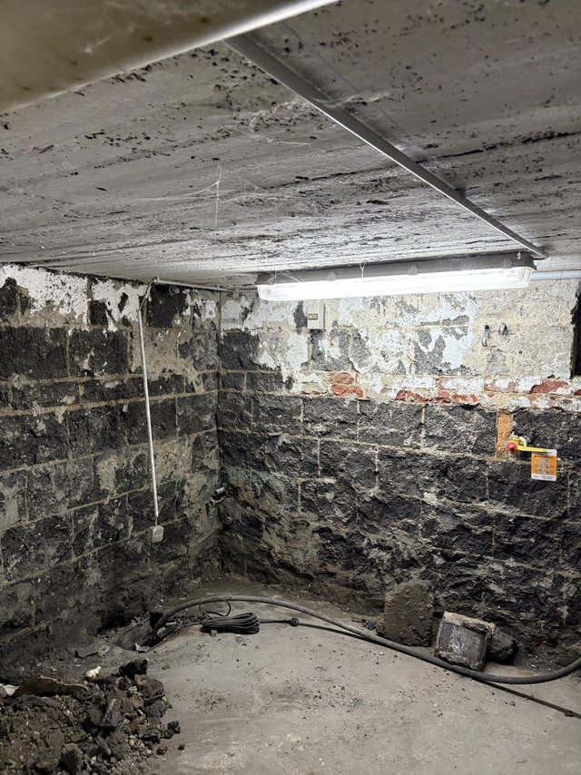 Freigelegte Kellerwand aus dunklem Mauerwerk mit abgeplatzter weißer Beschichtung.