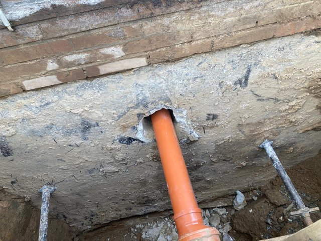 Orangefarbenes Rohr führt durch Bohrung in freigelegter Gebäudewand.