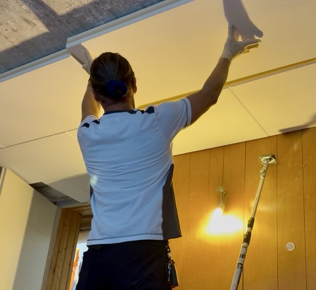 Person mit Handschuhen montiert weiße Deckenplatte an abgehängter Decke.