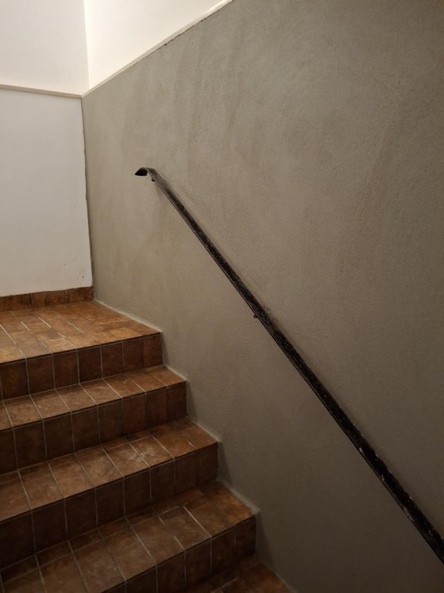 Geflieste Treppe im Treppenhaus mit schwarzem Handlauf und grauer Wand.