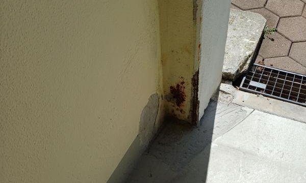 Flecken und abplatzende Beschichtung am Wandfuß in einer Balkonecke.