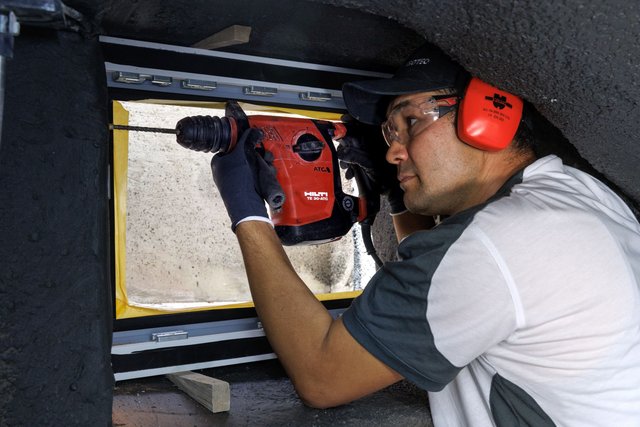 ISOTEC Mitarbeiter bohrt mit rotem Bohrhammer in Betonfläche, Schutzbrille und Gehörschutz.