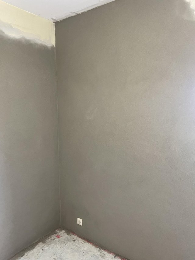 Zimmerecke mit frisch grauer Wandbeschichtung, Steckdose und abgedecktem Boden