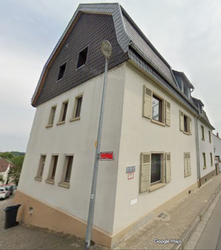 Straßenansicht eines mehrstöckigen Hauses mit Schieferdach und hellen Fensterläden.