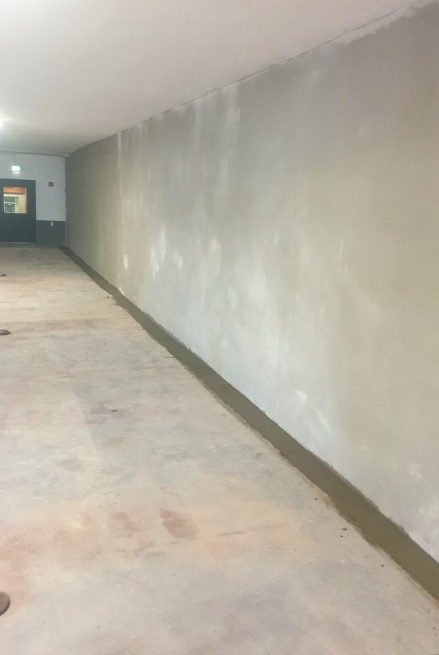 Lange Wand in Flur mit grauer Masse und dunklem Randstreifen am Boden