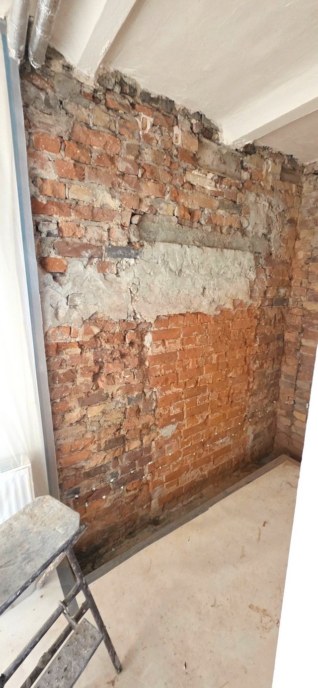 Freigelegte Ziegelwand mit bröckelndem Mörtel in schmalem Raum