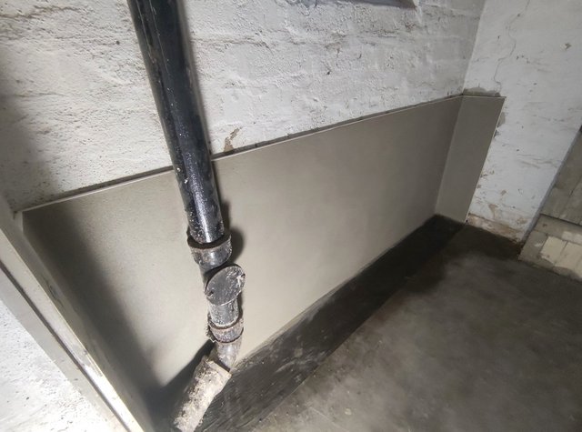 Helle Platte an Kellerwand montiert, schwarzes Rohr verläuft davor