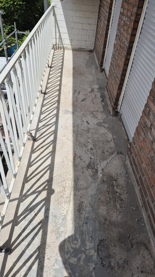 Abgeplatzter Betonboden auf schmalem Balkon mit Metallgeländer und Rollläden