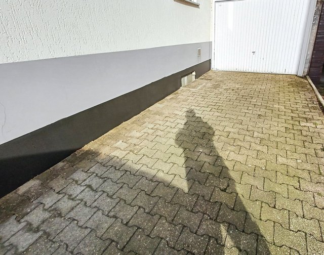 Schwarze Beschichtung am Sockel einer Hauswand neben gepflasterter Einfahrt und Garagentor
