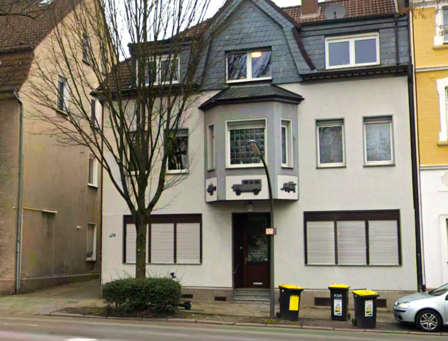 Mehrstöckiges Wohnhaus mit Erker, Straßenlaterne und Mülltonnen am Gehweg