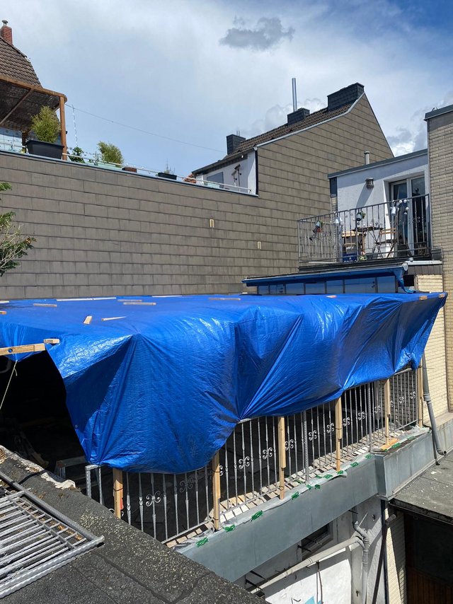 Blaue Plane deckt Balkon und Gerüst an Wohngebäude ab.