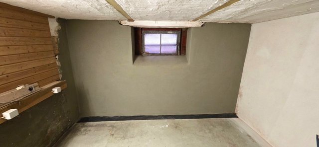 Kellerraum mit glatter grauer Wand und kleinem Fenster in der Wandnische.