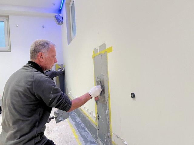 Arbeiter trägt graue Masse auf Kellerwand auf.