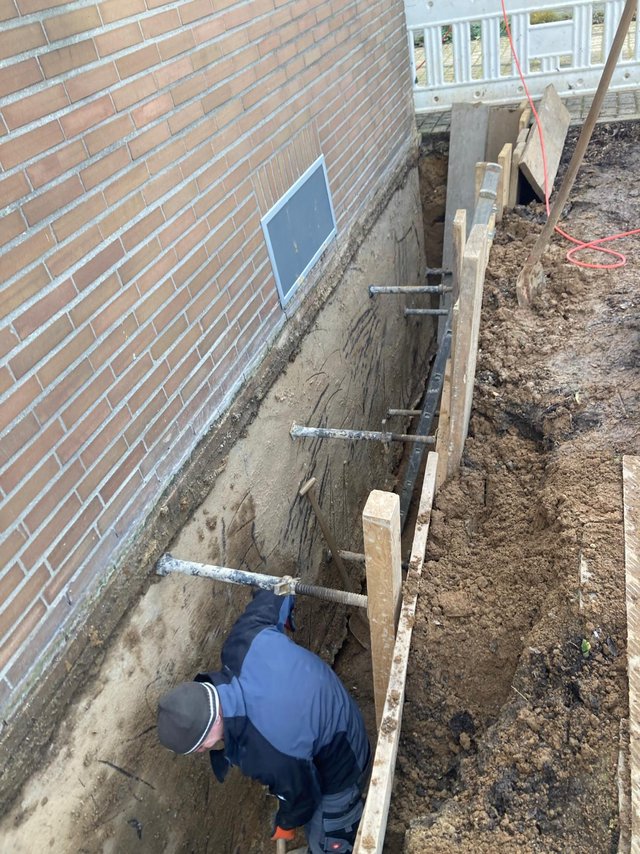 Arbeiter gräbt an freigelegter Gebäudewand im Erdreich.