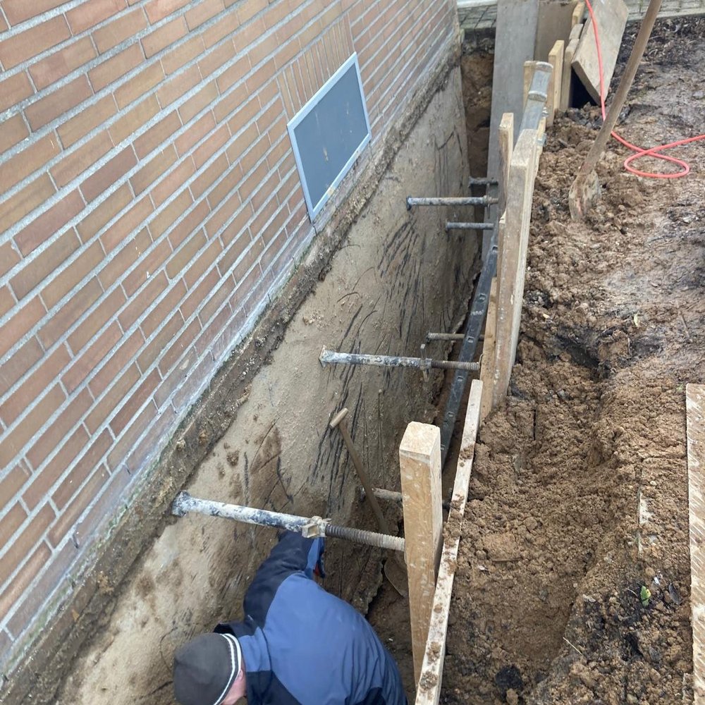 Arbeiter gräbt an freigelegter Gebäudewand im Erdreich.