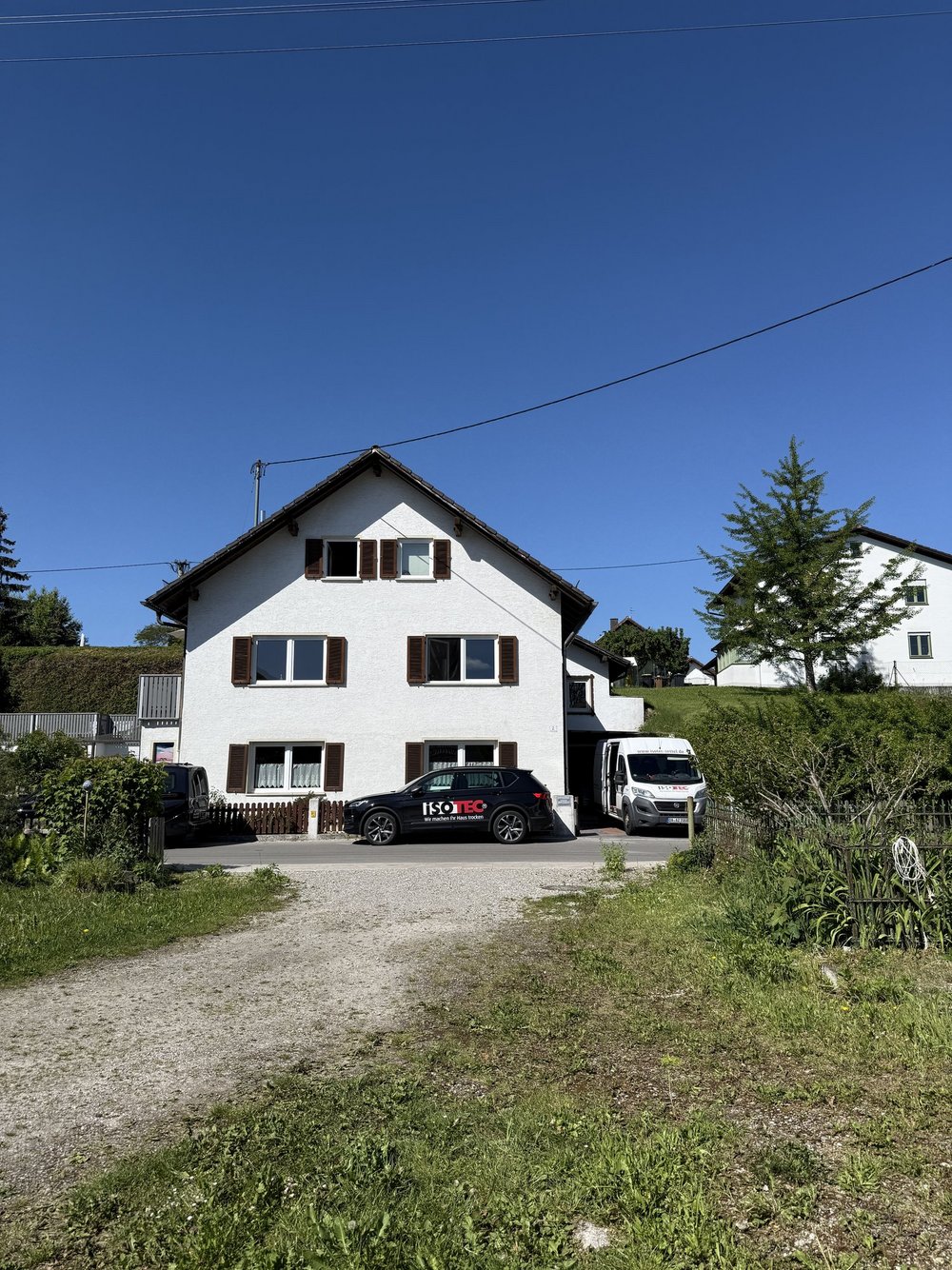 ISOTEC Fahrzeuge vor weißem Wohnhaus mit Garten und Zufahrt