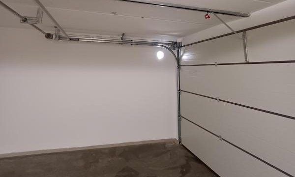 Leere Garage mit weißem Sektionaltor und Flecken auf dem Betonboden