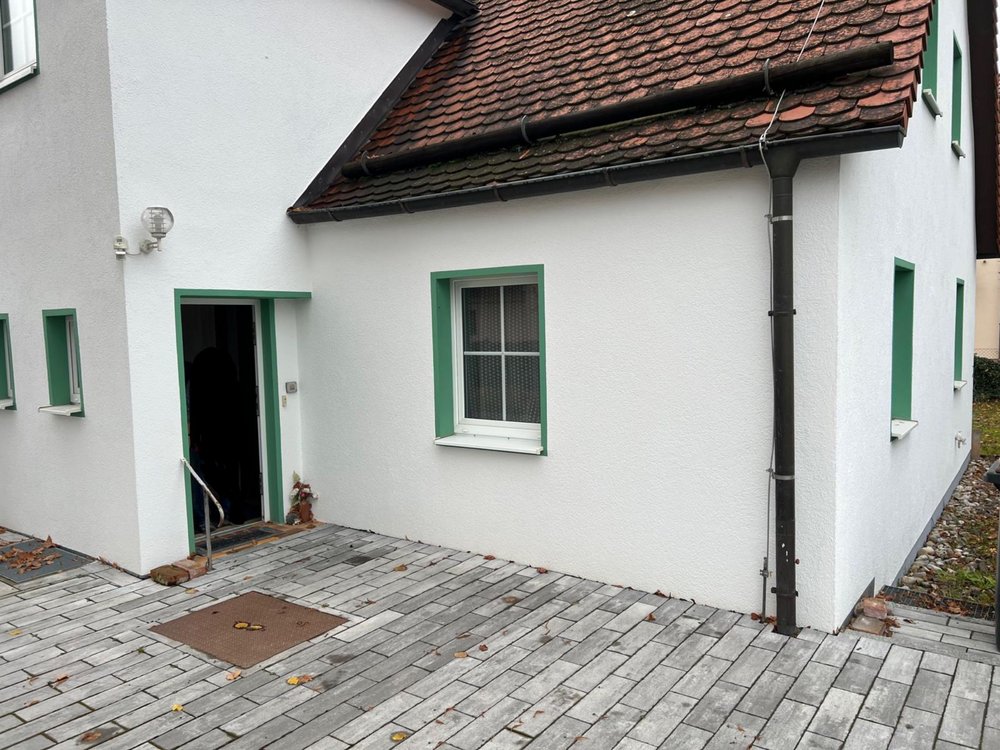 Weiße Hausfassade mit rotem Ziegeldach, Fallrohr und gepflastertem Eingangsbereich