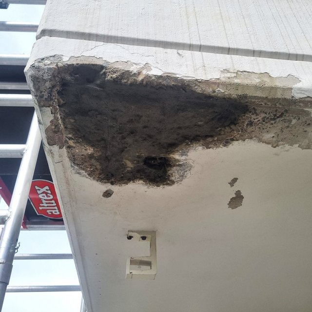 Abplatzung an Betonkante, graue Masse liegt frei, Risse sichtbar.