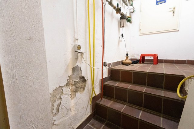 Abgeplatzte Wandbeschichtung mit freigelegtem Mauerwerk neben gefliester Kellertreppe