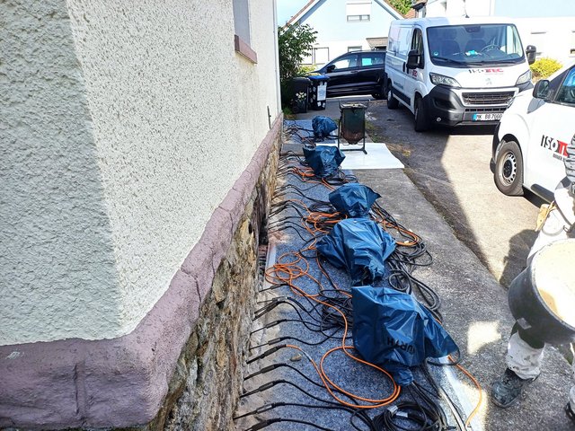 ISOTEC Mitarbeiter richtet verkabelte Geräte entlang Hauswand aus.