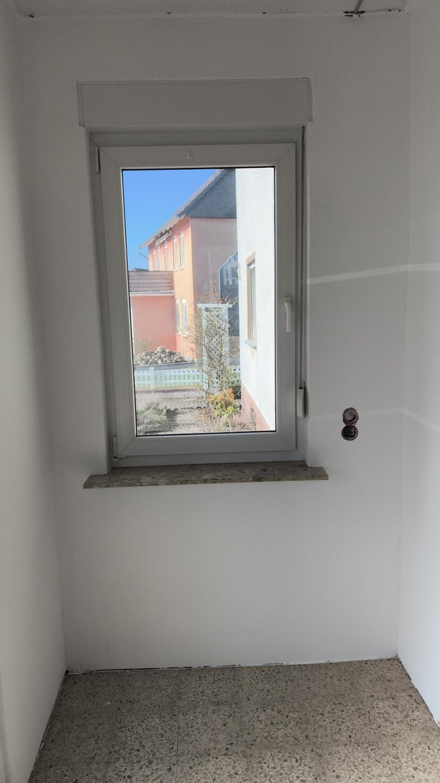 Leerer Raum mit Fenster, weißer Wand und freiliegender Steckdose
