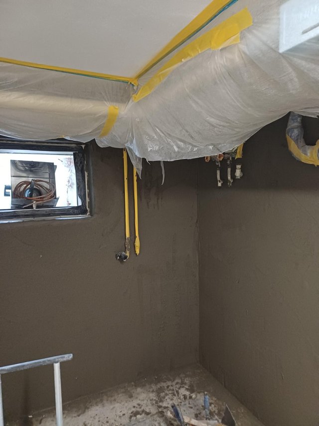 Abgeklebte Folie schützt Decke; graue Masse auf Wand, Fensteröffnung sichtbar.