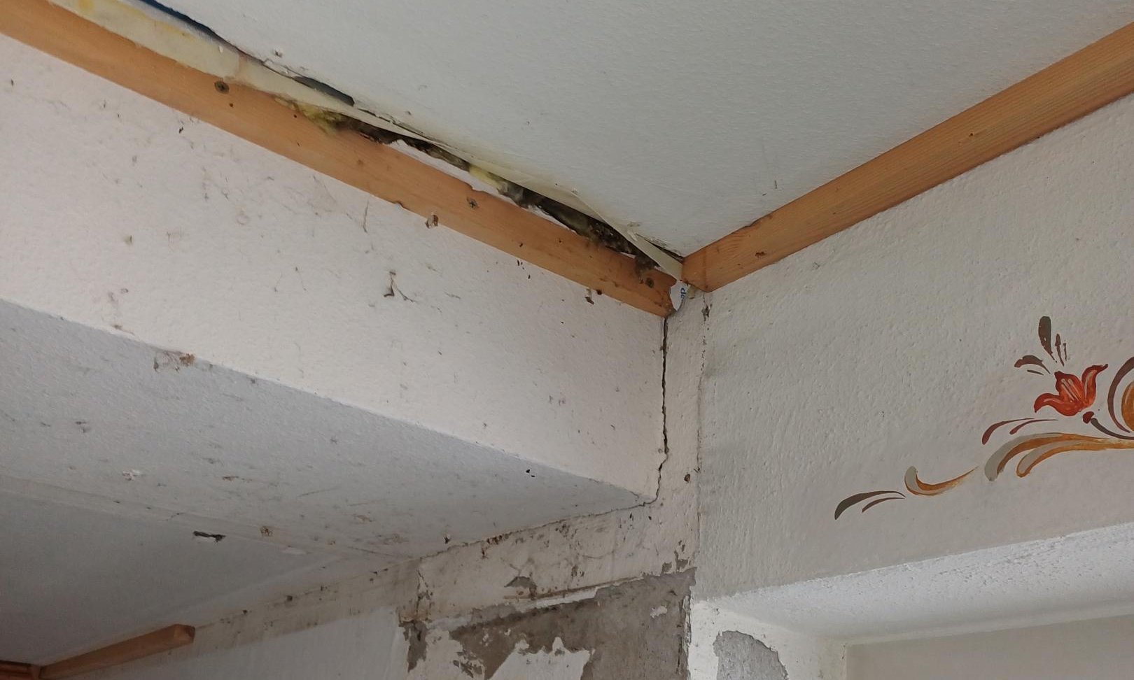 Beschädigte Wand- und Deckenecke mit freiliegender Dämmung und Rissen.