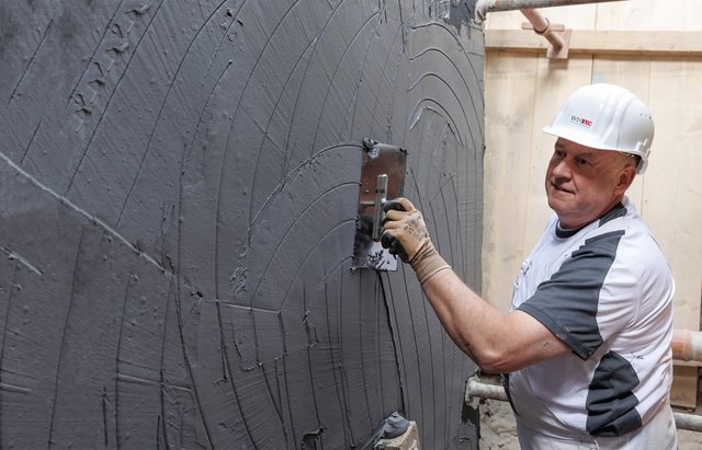ISOTEC Mitarbeiter trägt graue Masse auf Kellerwand auf.