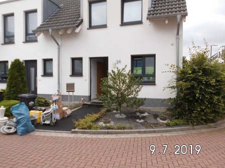 Hauseingang mit weißen Werkzeugen, Kartons und Schläuchen vor einem Wohnhaus.