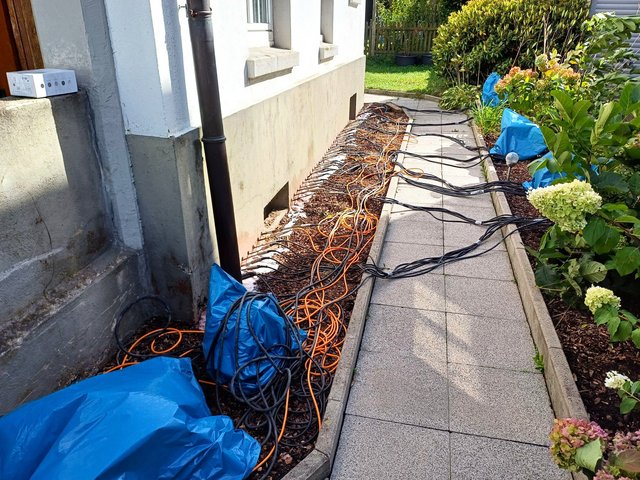 Kabelstränge liegen entlang der Hausfassade im Gartenbereich.