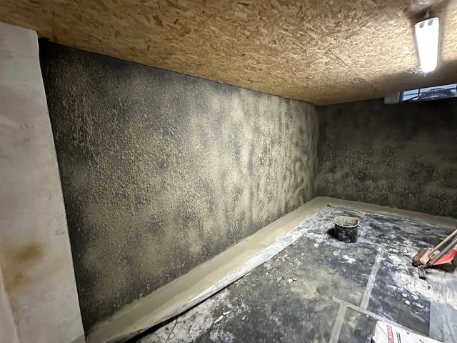 Schimmelbefall an Kellerwand, Folienabdeckung und Eimer im Vordergrund