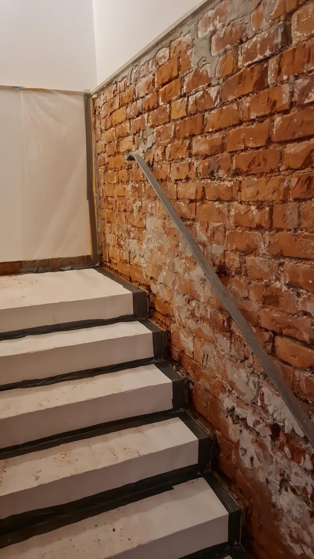 Treppenhaus mit freigelegter Ziegelwand, weiße Ausblühungen und Metallhandlauf