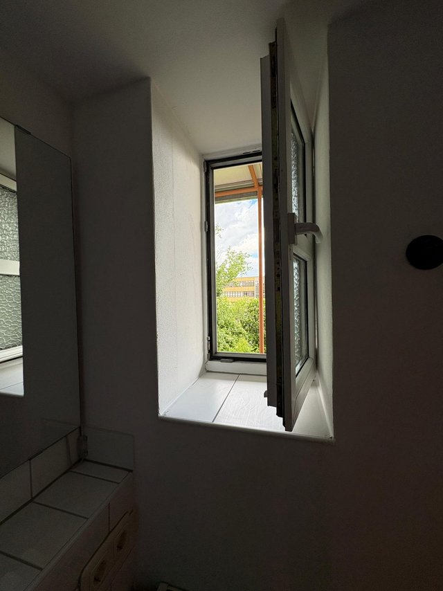 Offenes Fenster in schmalem Raum, Ausblick auf Bäume und Gebäude