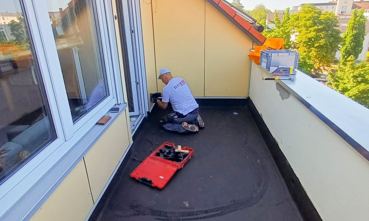 ISOTEC Mitarbeiter arbeitet kniend an einem Balkonanschluss neben Fenster und Tür.