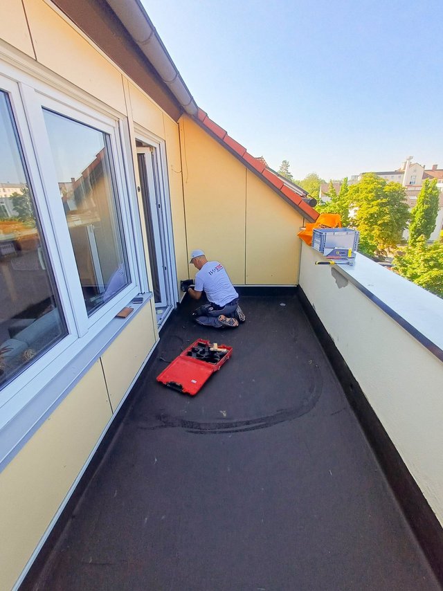 ISOTEC Mitarbeiter arbeitet kniend an einem Balkonanschluss neben Fenster und Tür.