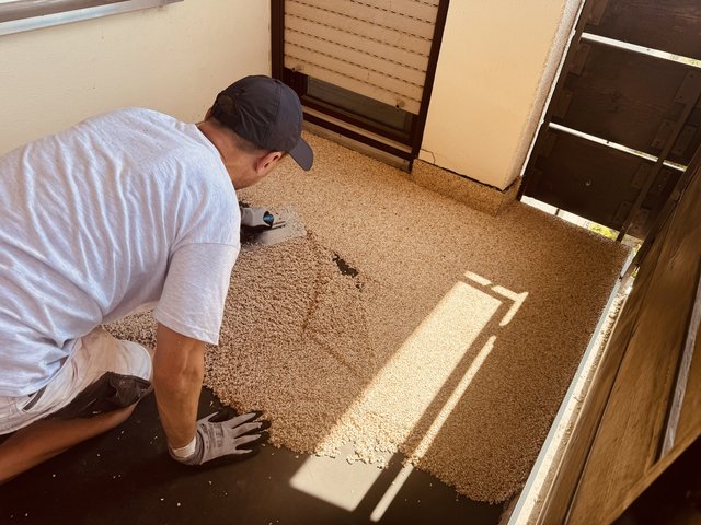 Arbeiter verteilt helle Steinchen auf Balkonboden mit Glättkelle.