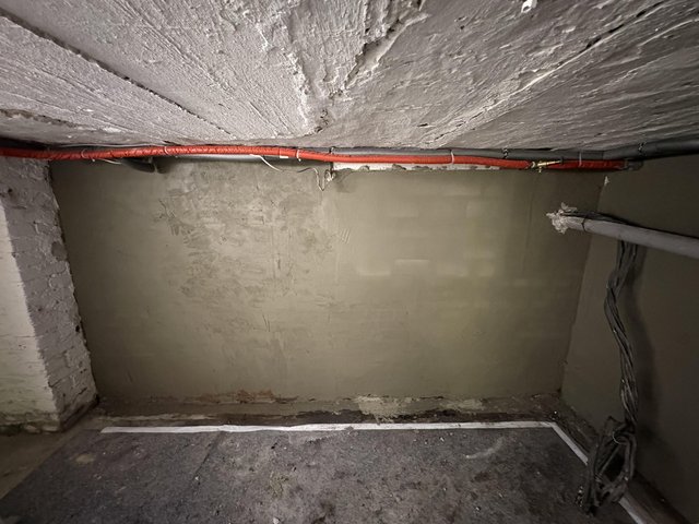Graue Kellerwand mit frischer Masse unter rohrverkleideter Betondecke