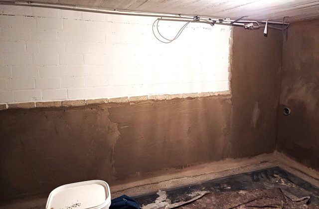 Kellerwand mit brauner Masse im Sockelbereich, freigelegte Mauersteine darüber